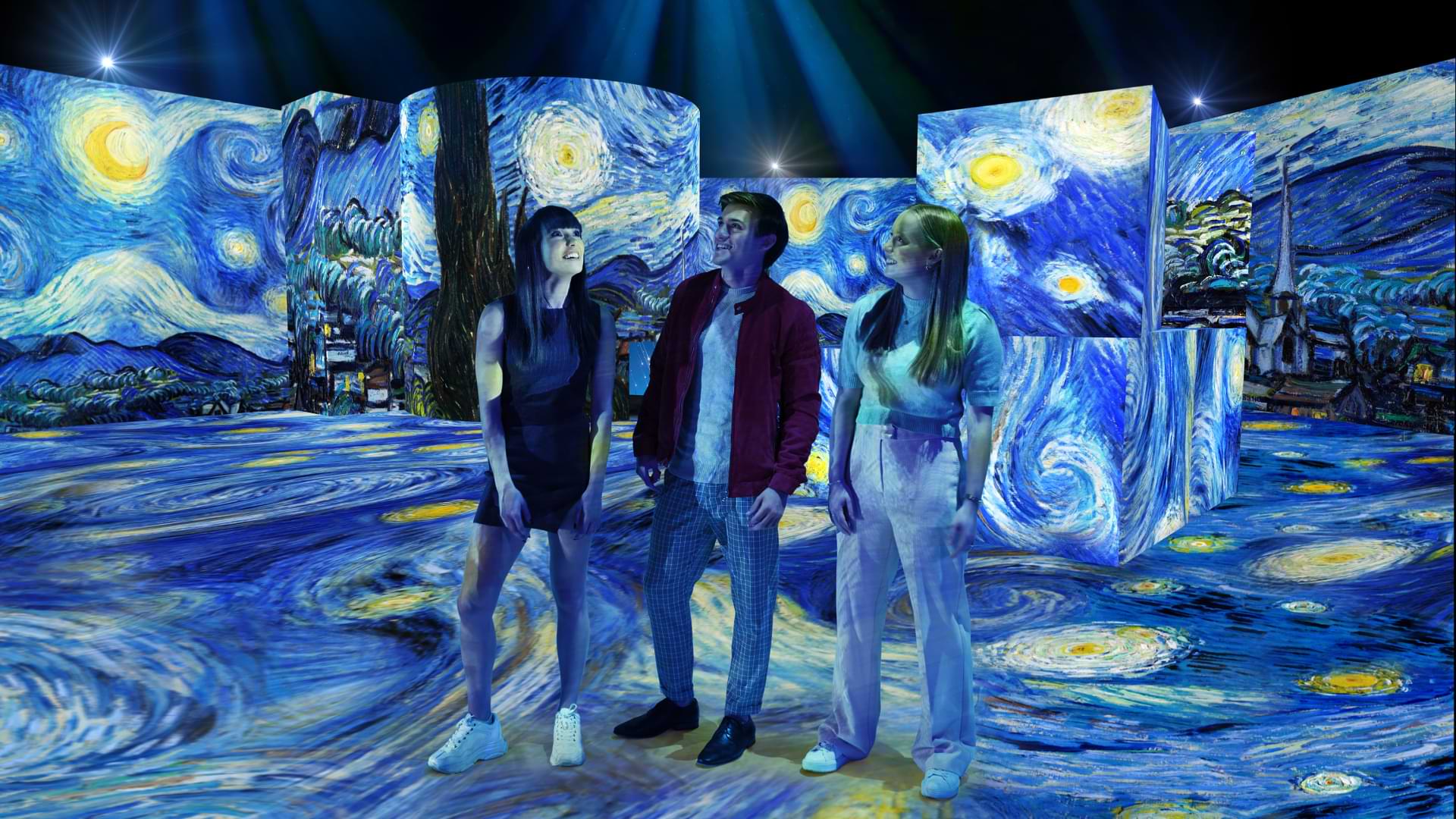 A girl, boy and another girl stand in the Van Gogh Alive exhibition - with Van Gogh's Starry Night projected on every surface of the exhibition.