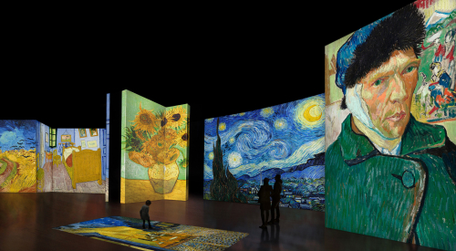 Child stands on an illuminated Van Gogh artwork on the floor, two adults look at screens.