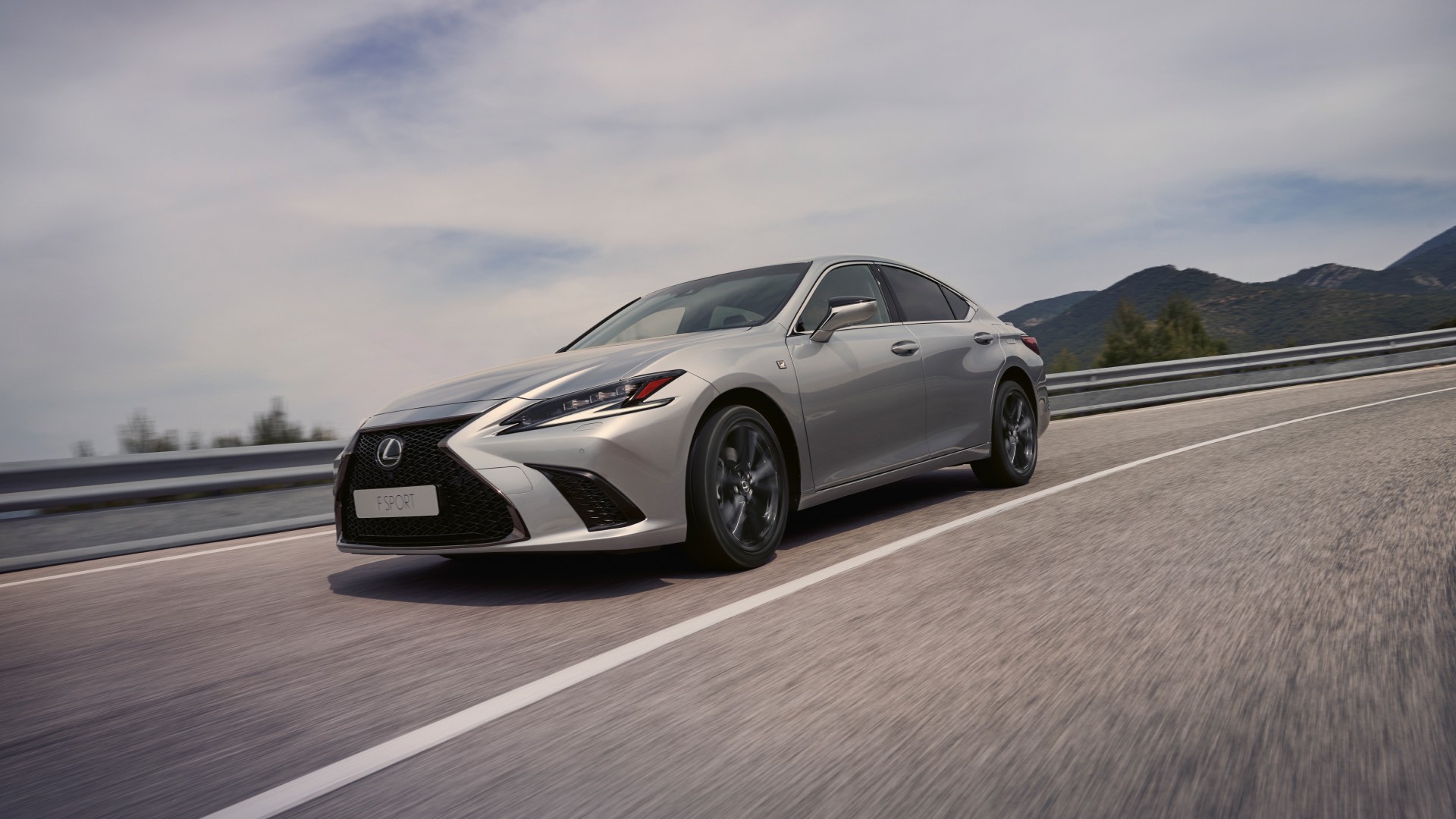 The side, low view of a silver Lexus ES F Sport as it speeds along a highway.