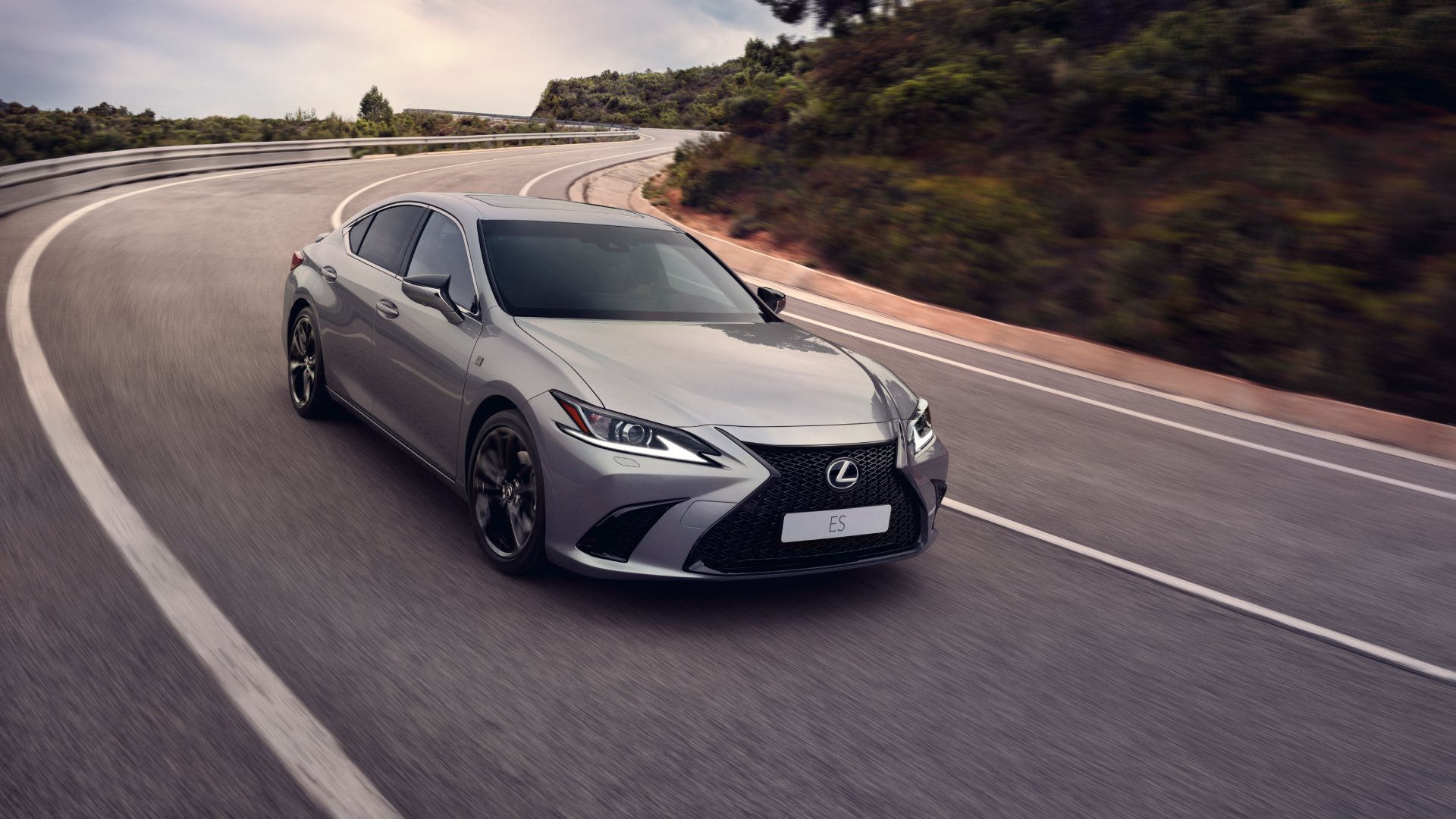 A high, side view of a silver Lexus ES F Sport as it speeds along a windy highway.
